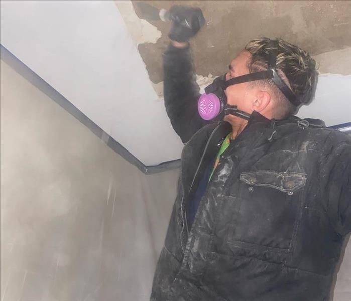 Technician with respirator scrapes away paint for ceiling water cleanup