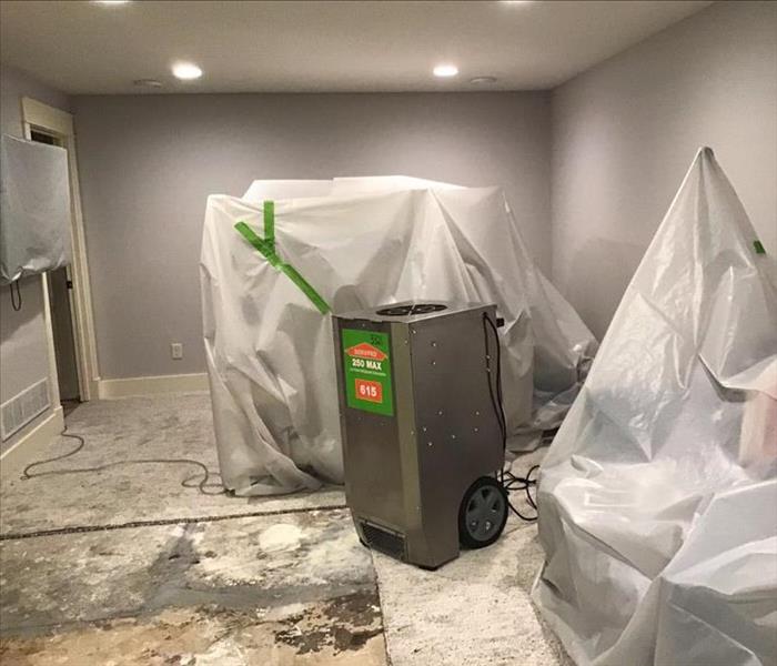 stainless steel dehumidifier in a water damaged room with plastic covering the furniture